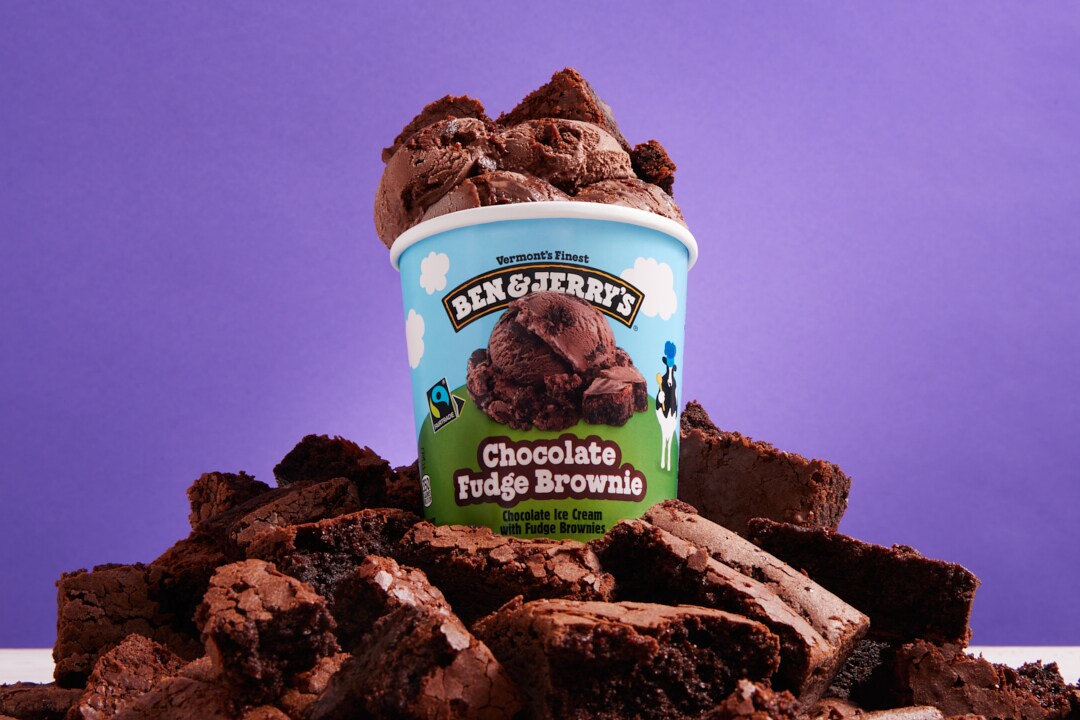Pint of Ben & Jerry's Chocolate Fudge Brownie ice cream surrounded by brownies. Purple background.