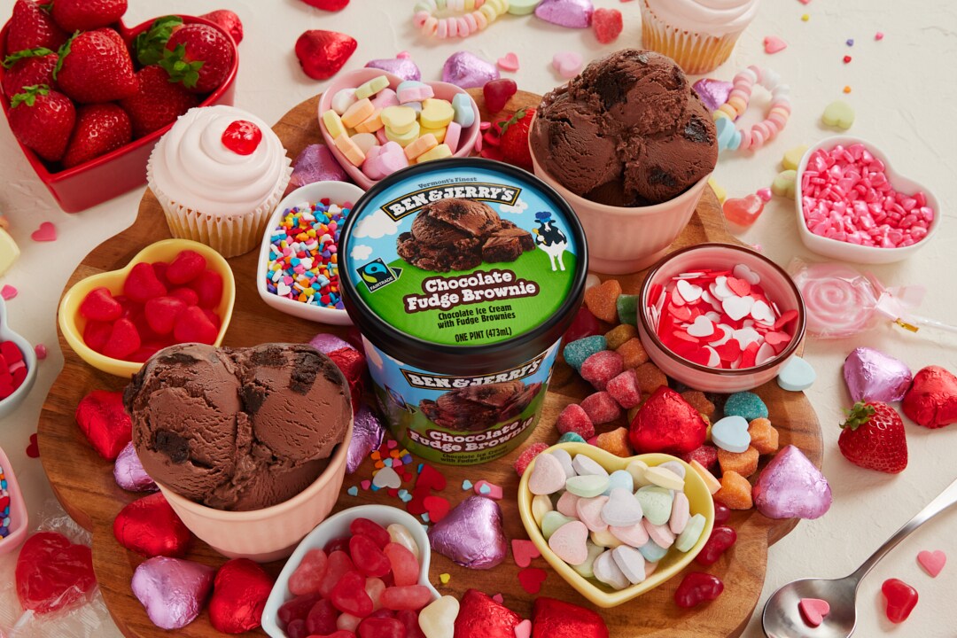 Pint of Ben & Jerry's Chocolate Fudge Brownie ice cream surrounded by bowls of scooped ice cream and Valentine's Day decor.
