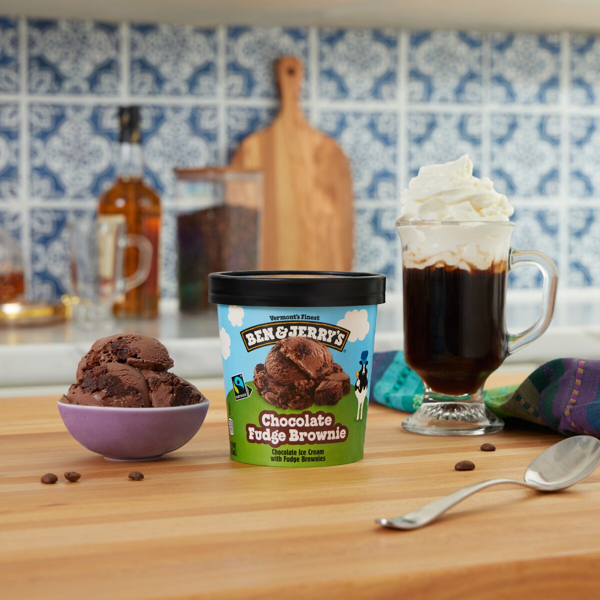 Pint of Ben & Jerry's Chocolate Fudge Brownie ice cream next to a mug of Irish coffee with whipped cream in a kitchen setting.