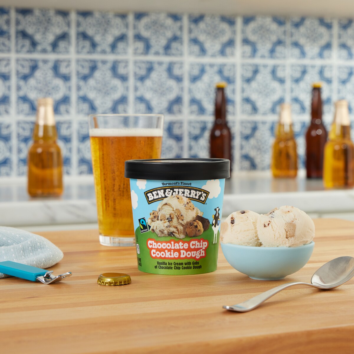 Pint of Ben & Jerry's Chocolate Chip Cookie Dough ice cream next to a pint of lager in a kitchen setting.