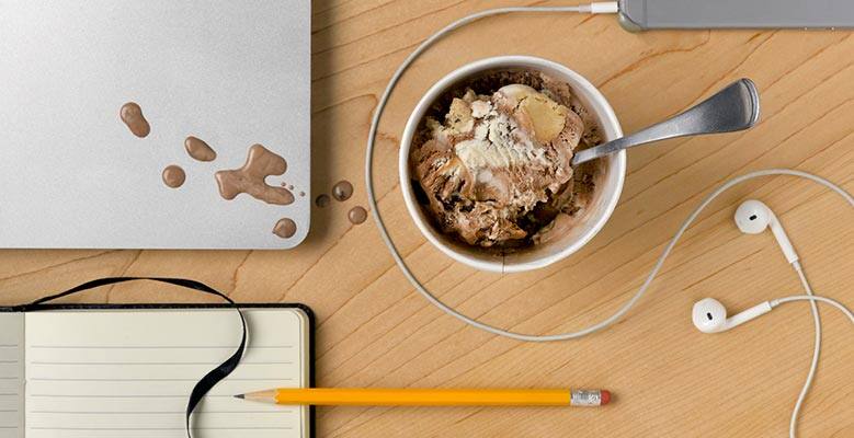 Pint of Ben & Jerry's ice cream on a desk with computer, notebook, pencil.