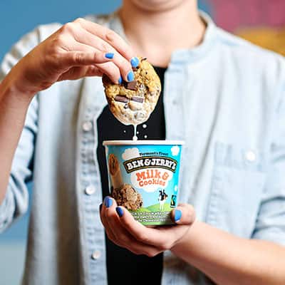 A cookie dripping with milk coming out of a pint of Ben & Jerry's Milk & Cookies Ice Cream
