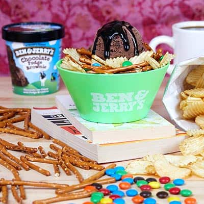 A pint of ice cream, pretzels, potato chips and candy on desk along with the finished sundae