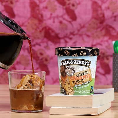 A pint of ice cream with a glass with ice cream and coffee being poured into it