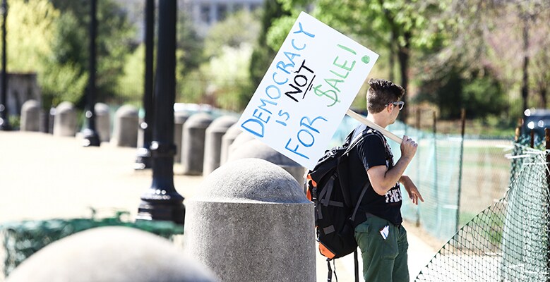 someone holding sign that says Democracy is not for sale