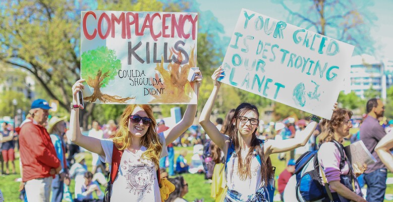 two people holding signs that say Complacency Kills - coulda, shoulda, didn't and  Your greed is destroying our planet