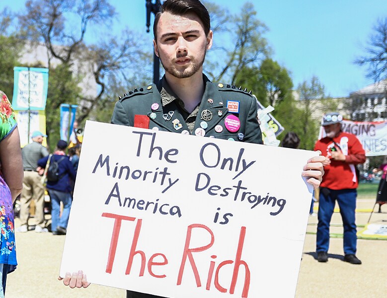 someone holding sign that says The Only Minority Destroying America is The Rich 