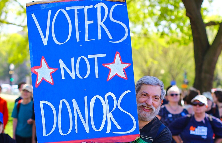 Crowd with someone holding a sign that says Voters not Donors