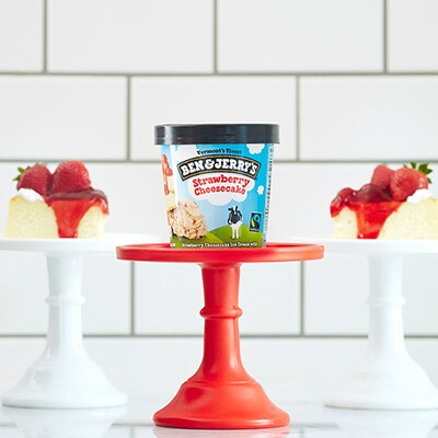 Ben & Jerry's Strawberry Cheesecake ice cream on a pedestal next to cheesecakes