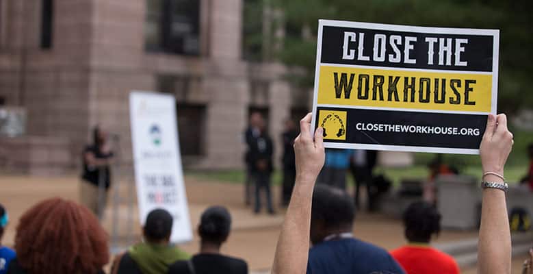 Hands holding sign that says "Close the Workhouse!"