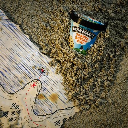 A pint of Ben & Jerry's Peanut Butter Cup buried in sand