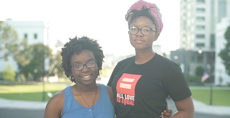 A same sex couple standing arm in arm